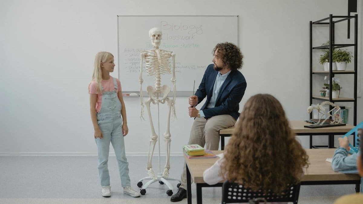 Teacher and students in a classroom using a skeleton model for a biology lesson.