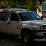 A white Dodge Ram pickup truck parked in a shaded driveway beside a house.