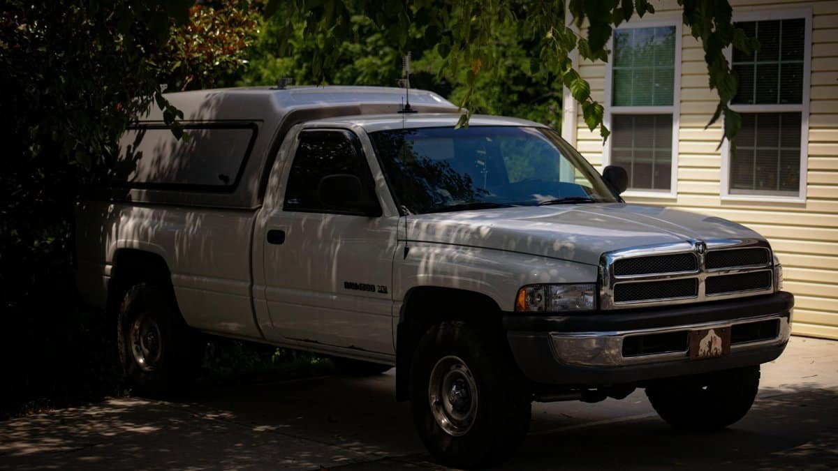 A white Dodge Ram pickup truck parked in a shaded driveway beside a house.
