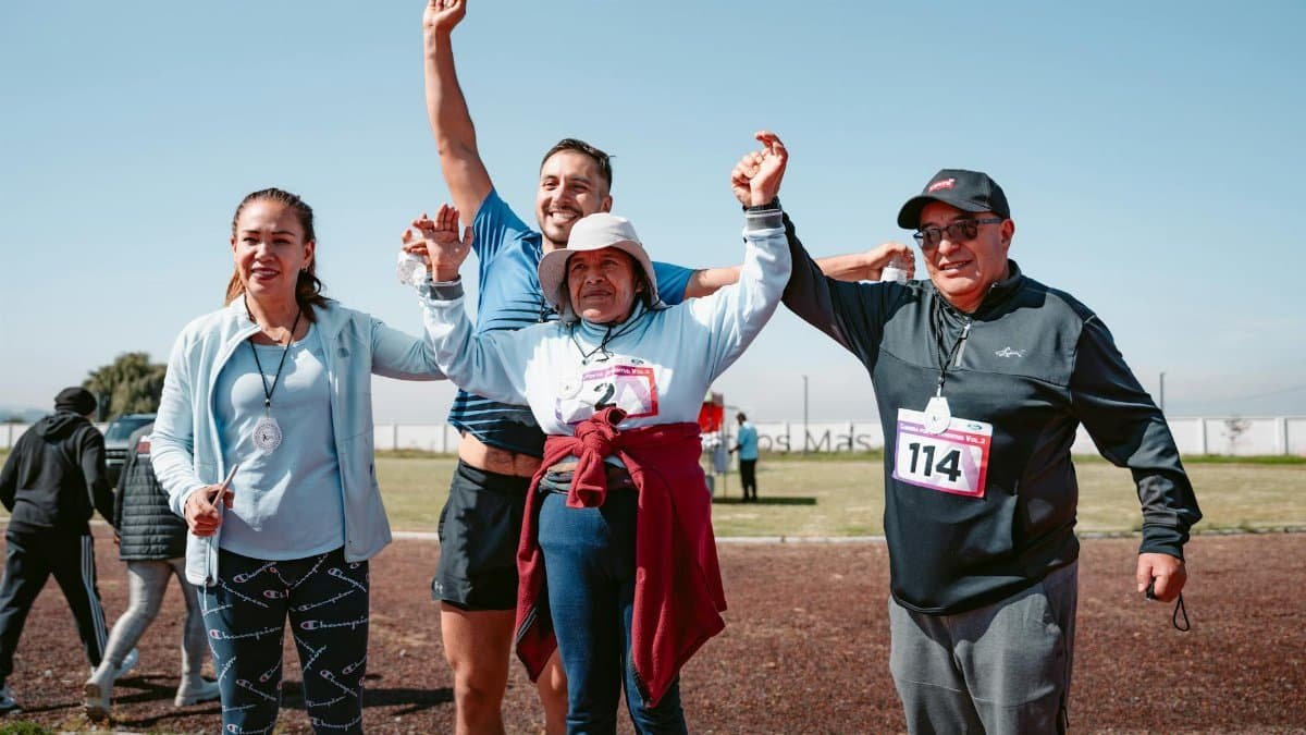 Four adults joyfully celebrating after completing a race, holding medals outdoors.