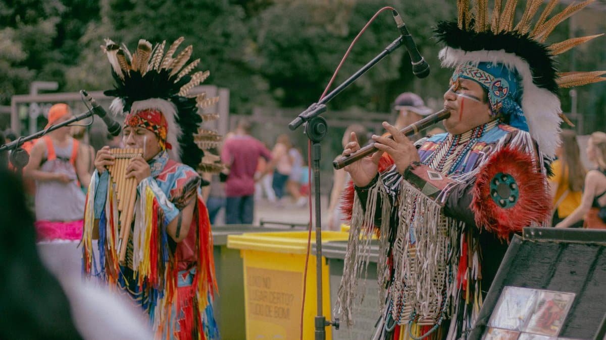 Native American musicians performing outdoors in traditional wear with woodwind instruments.