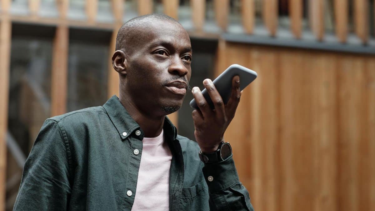 Stylish adult man using his smartphone for voice commands in an outdoor urban setting.
