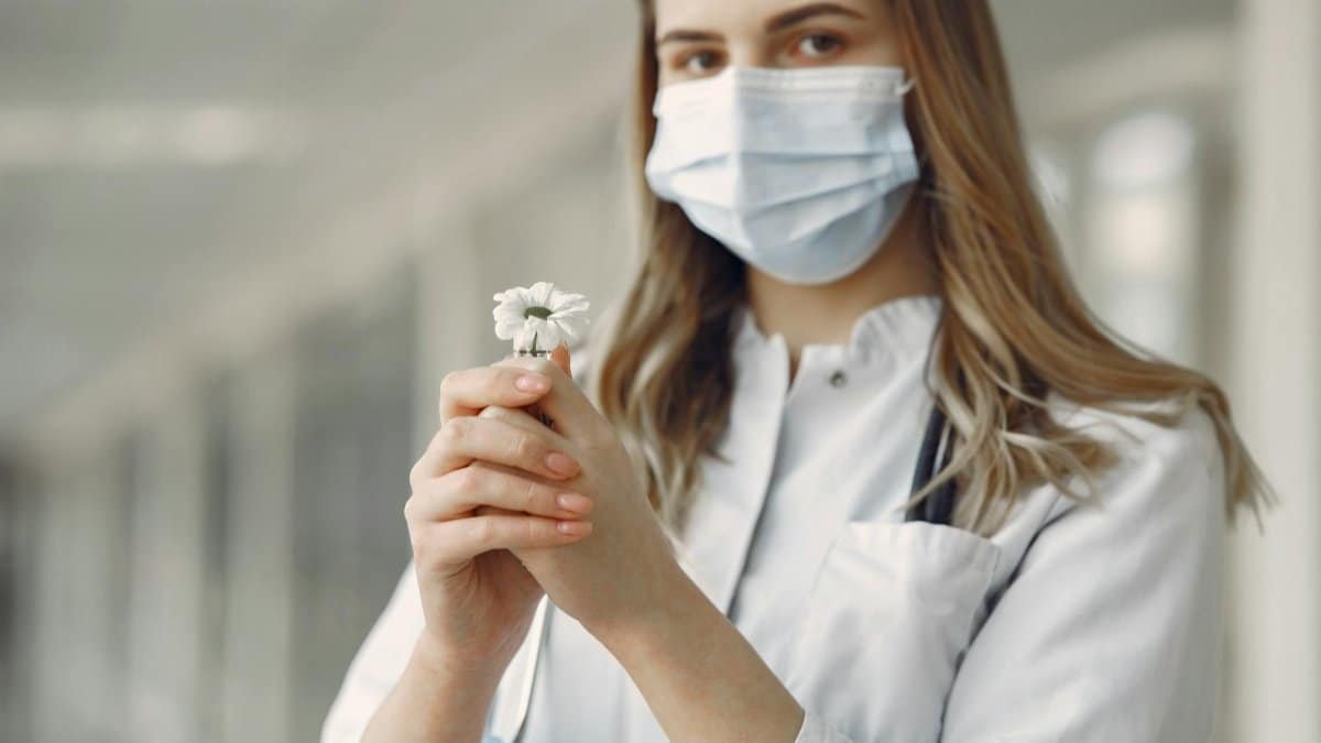 A young healthcare worker with a face mask holding a white flower, symbolizing hope and care.