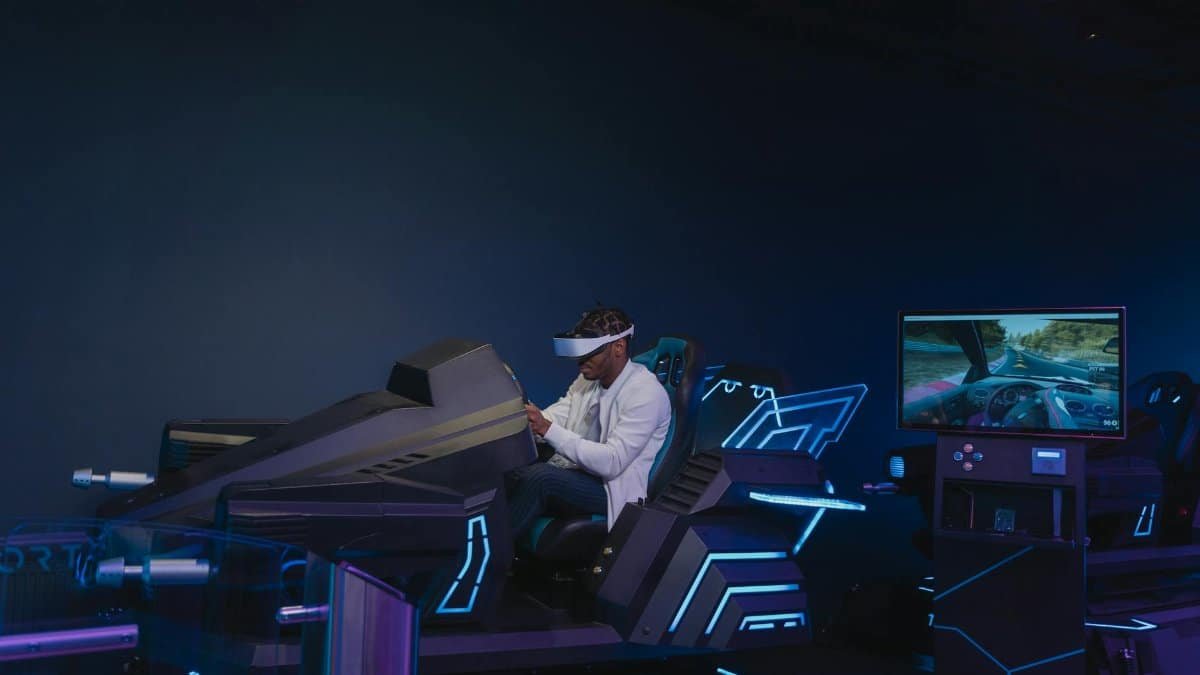 A young man immersed in a virtual reality driving simulation, wearing a VR headset indoors.