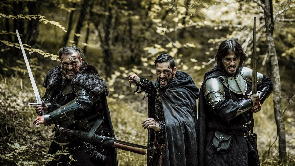 Three men in medieval armor and swords standing in a forest, ready for battle.