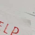 A raw and emotional depiction of a plea for help written on torn paper amidst lined sheets.