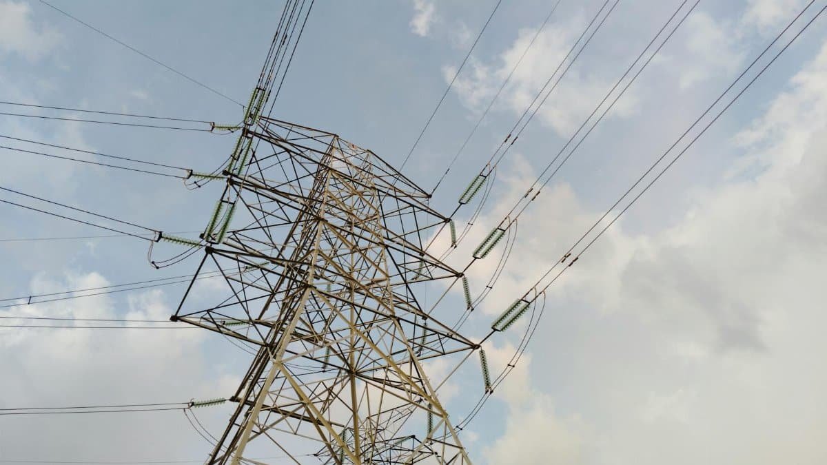 A close-up view of a high voltage transmission tower and lines against a cloudy sky.