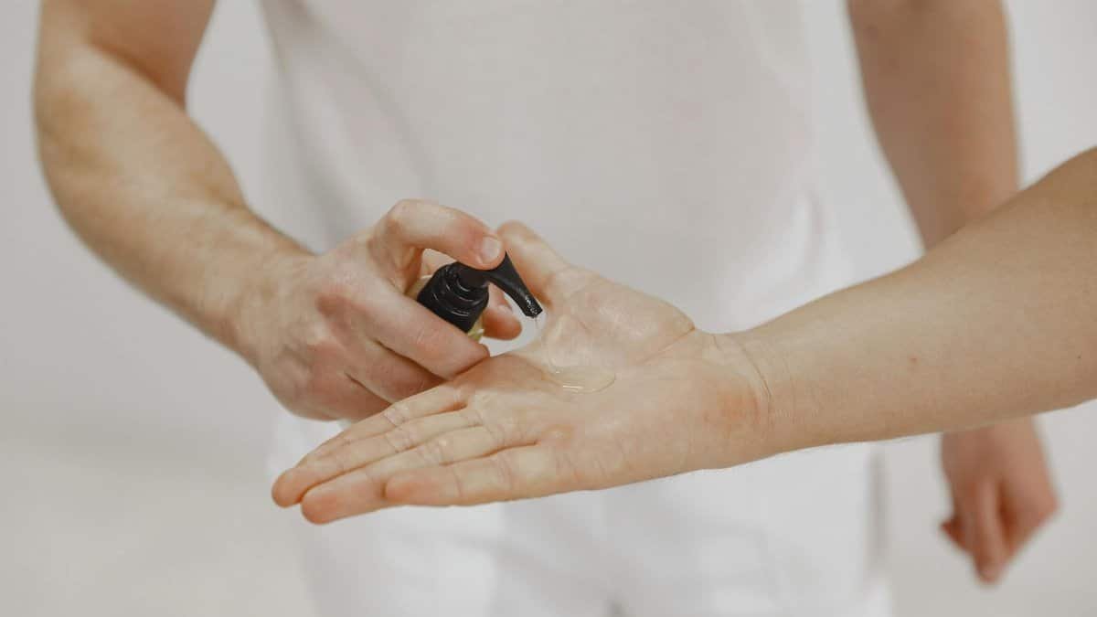 A close-up image of hands applying skincare oil from a pump bottle indoors.