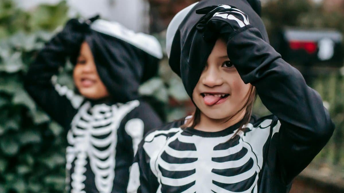 Two children in skeleton costumes having fun outdoors during Halloween.
