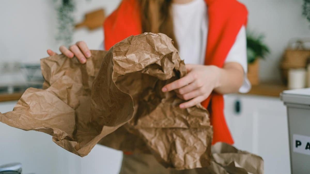 Young woman sorting crumpled paper for recycling in her kitchen to promote eco-friendly practices.