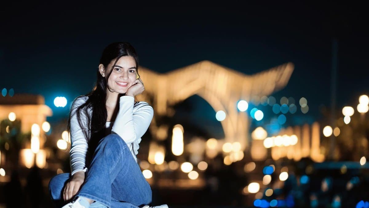 Portrait of a young woman smiling outdoors at night with city lights in the background.