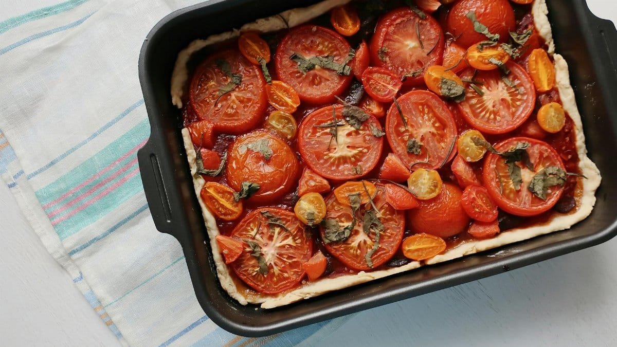 Top view of a freshly baked tomato tart with herbs and cherry tomatoes.