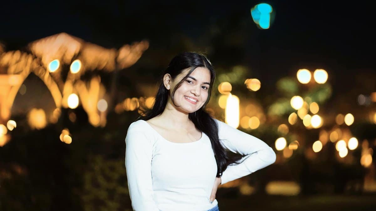 Smiling woman poses in a nighttime cityscape with blurred lights.