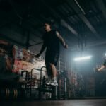 Two men actively skipping jump ropes in a dimly lit gym environment.