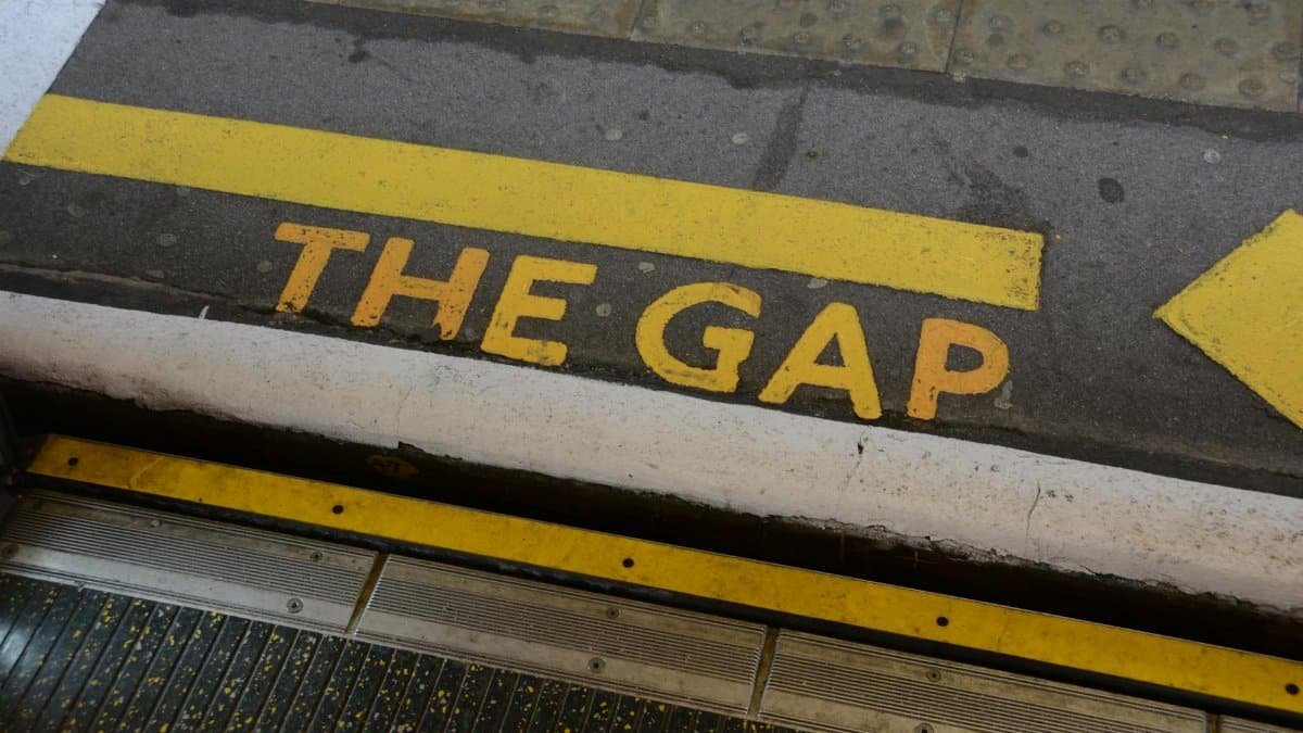 Close-up of 'Mind the Gap' warning sign on station platform edge, focusing on safety.