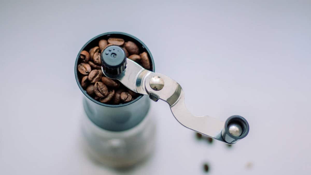 Top view of a manual coffee grinder filled with fresh coffee beans.