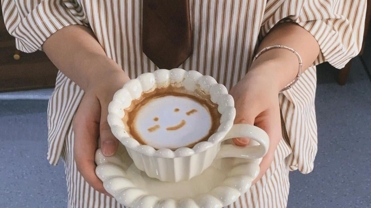 Latte with smiley face art in a white cup held by a woman.