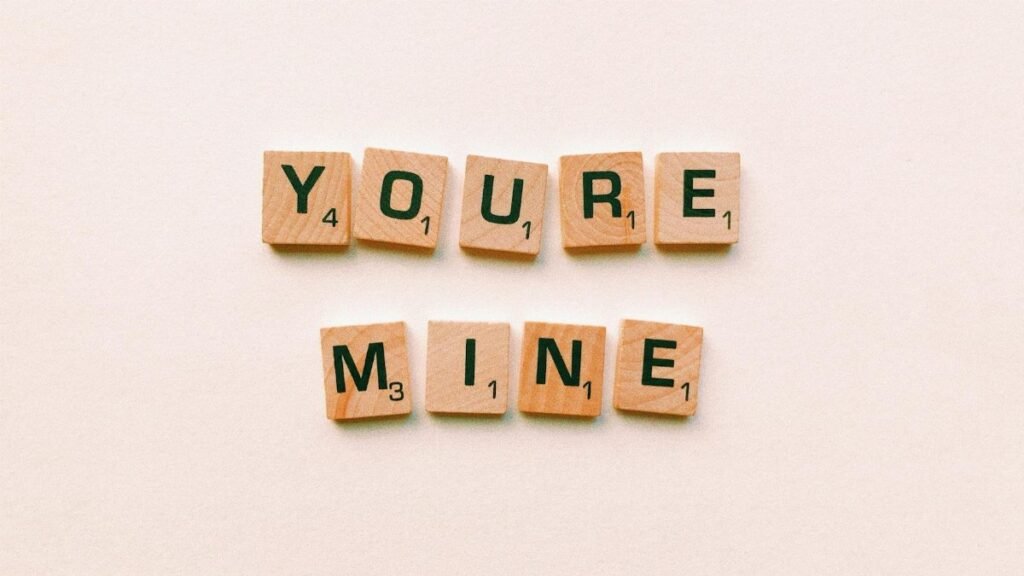 Romantic message You're Mine created with wooden Scrabble tiles on a pink background.