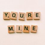 Romantic message You're Mine created with wooden Scrabble tiles on a pink background.