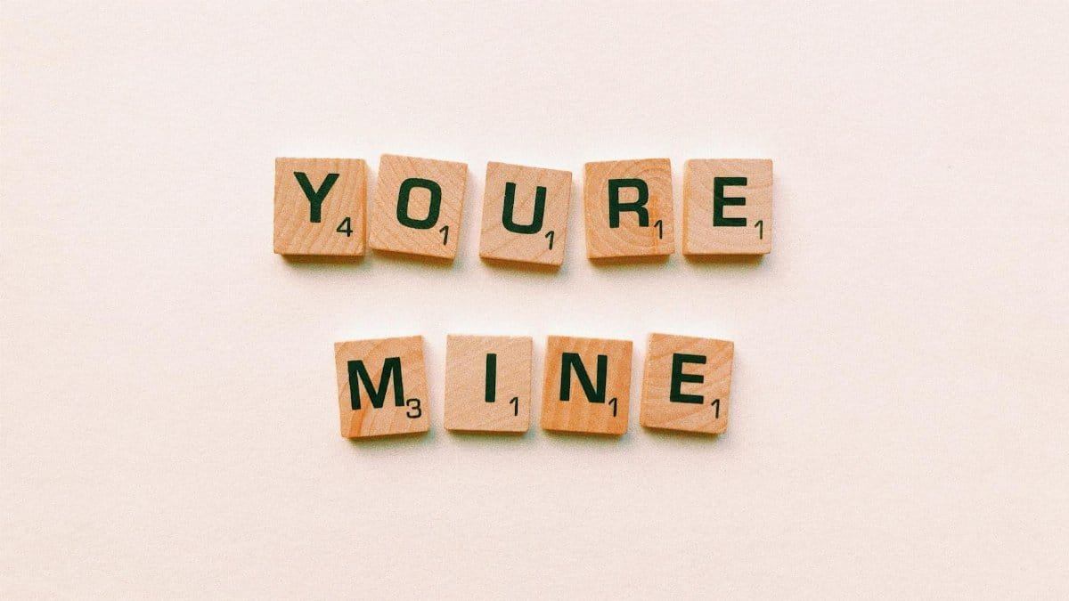 Romantic message You're Mine created with wooden Scrabble tiles on a pink background.