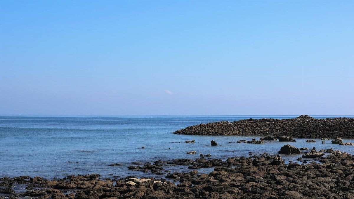A serene view of a rocky seashore under a clear blue sky in Cox's Bazar, Bangladesh.