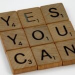 Wooden Scrabble tiles on white surface spelling 'Yes You Can,' promoting positivity and motivation.
