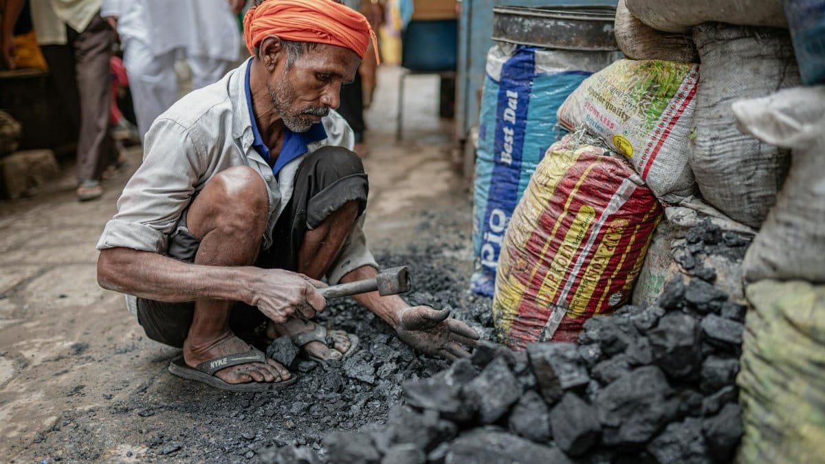 Mature man wearing turban sorts coal in an outdoor street market setting.