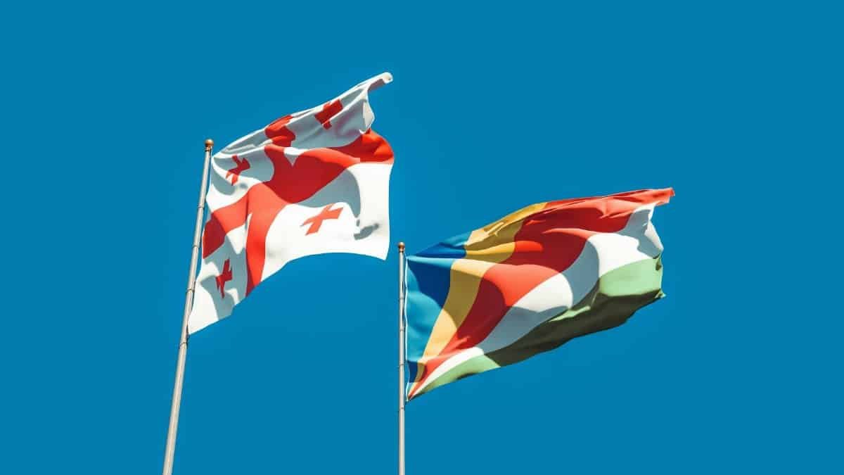 Vibrant image of Georgia and Seychelles flags waving with blue sky backdrop, symbolizing unity and cultural pride.