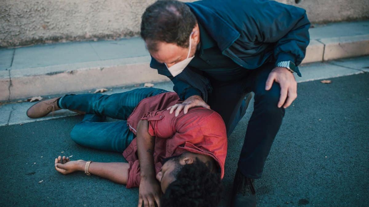 Paramedic aiding an injured man lying on the roadside, showcasing emergency care.