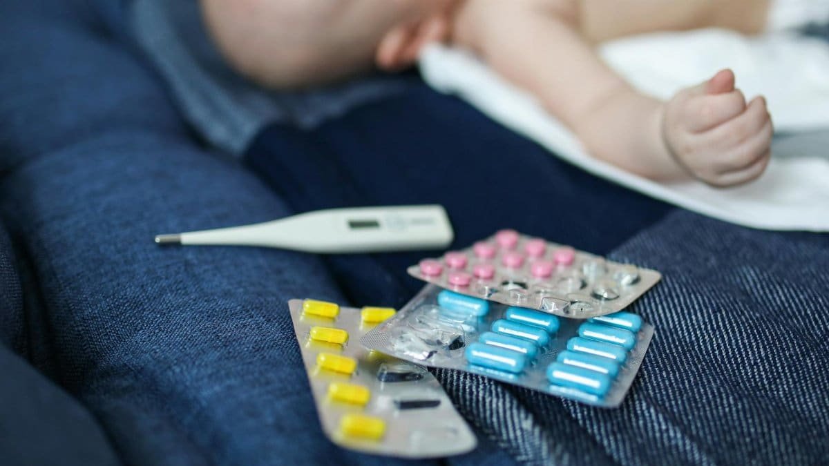 A baby lying next to various medications and a thermometer, suggesting health issues.