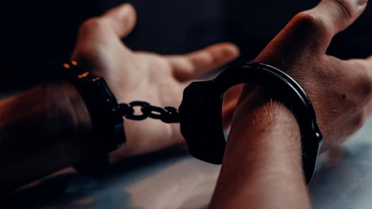 A close-up of human hands handcuffed on a table with a dark background, depicting law enforcement themes.