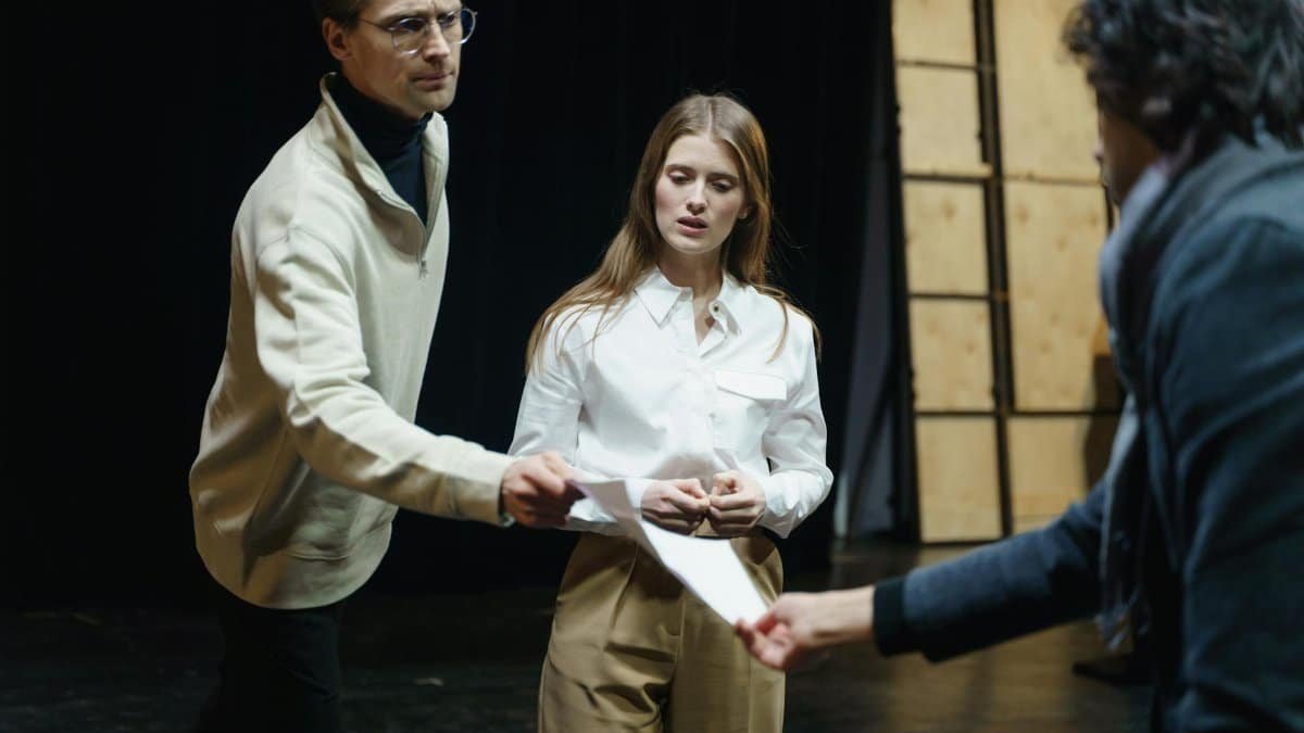 Actors engage in a rehearsal, exchanging scripts on stage, embodying theatrical drama and emotion.