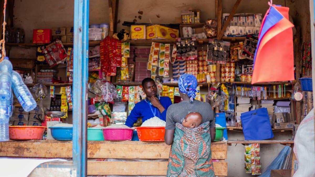 A woman with a baby in a wrap shops at a vibrant traditional market stall.