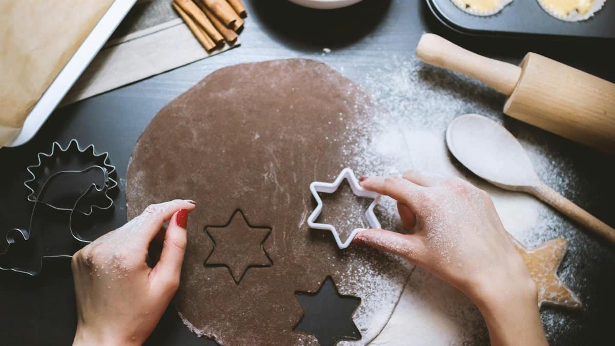 Hands cutting star-shaped cookies from chocolate dough, surrounded by baking tools.