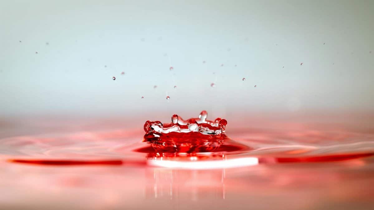 Close-up photo of a red water droplet creating ripples, showcasing fluid dynamics.