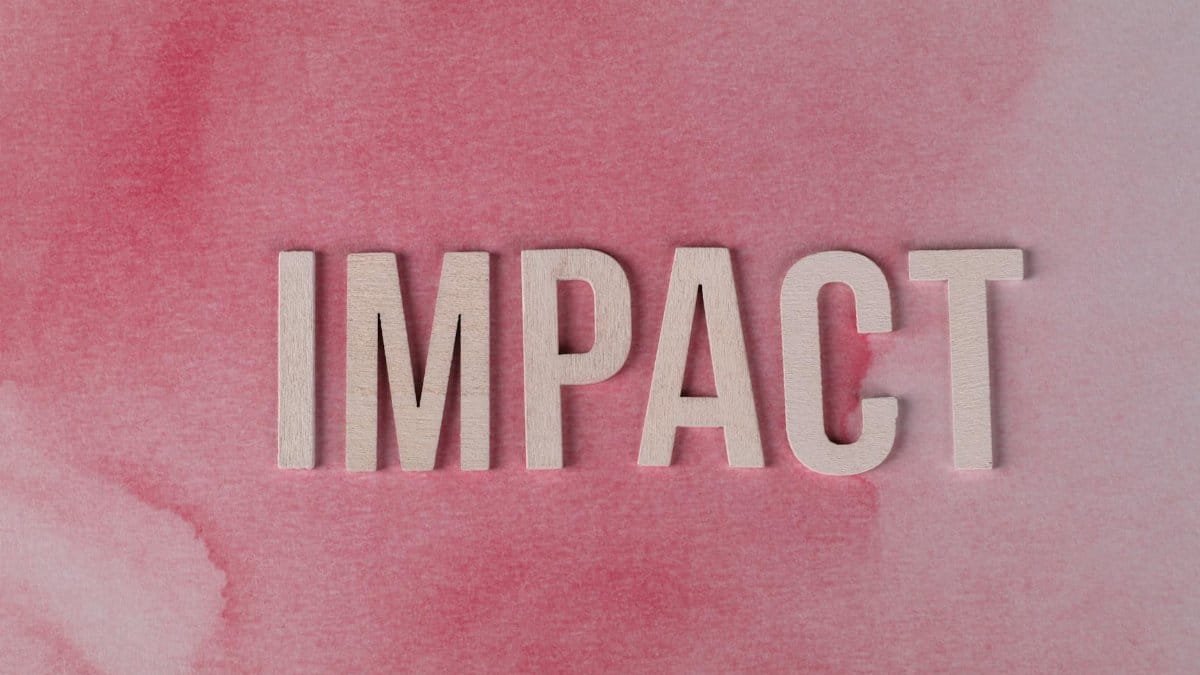 Wooden letters spelling 'IMPACT' against a textured pink watercolor backdrop, symbolizing influence and change.