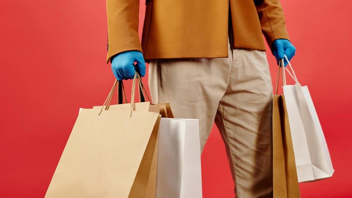Person with shopping bags and stylish attire against a red background, conveying modern consumerism.