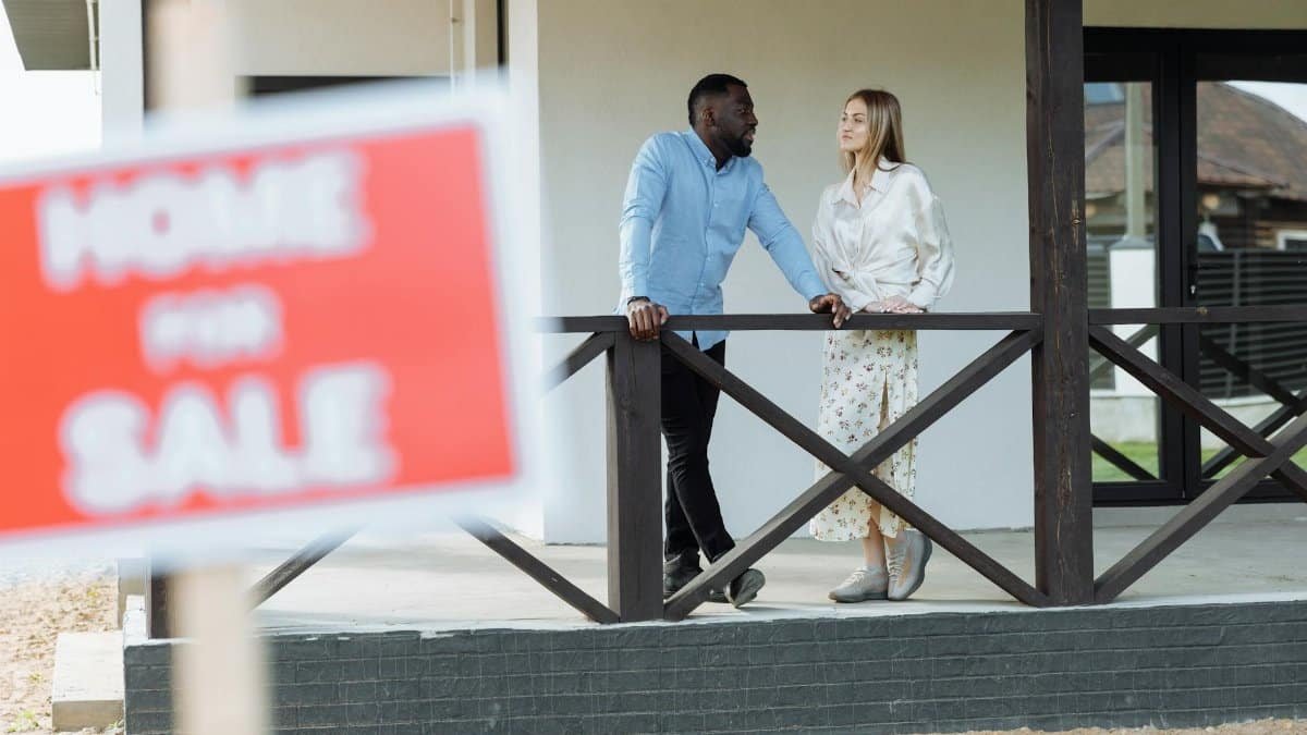 A black man and caucasian woman discussing a property for sale on a porch. Ideal for real estate content.