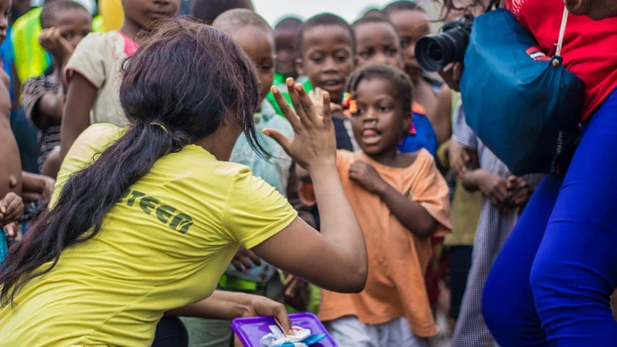 A woman engages with children through a high-five in a vibrant community setting.