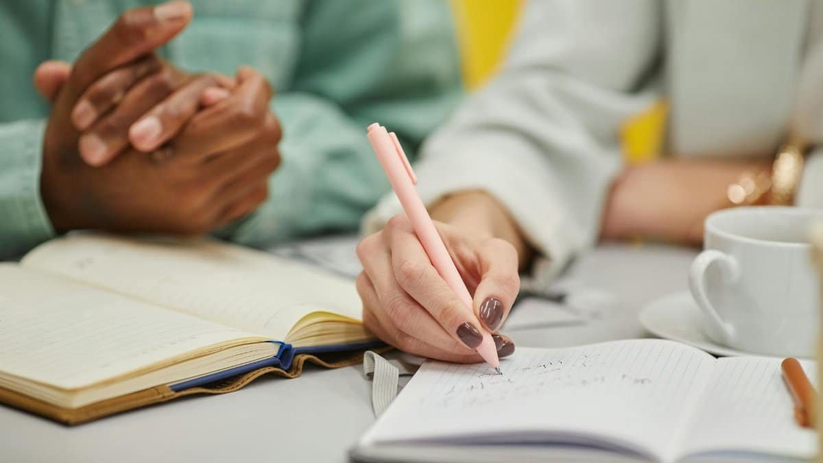 Close-up of diverse hands writing in notebooks with a pen during a meeting.