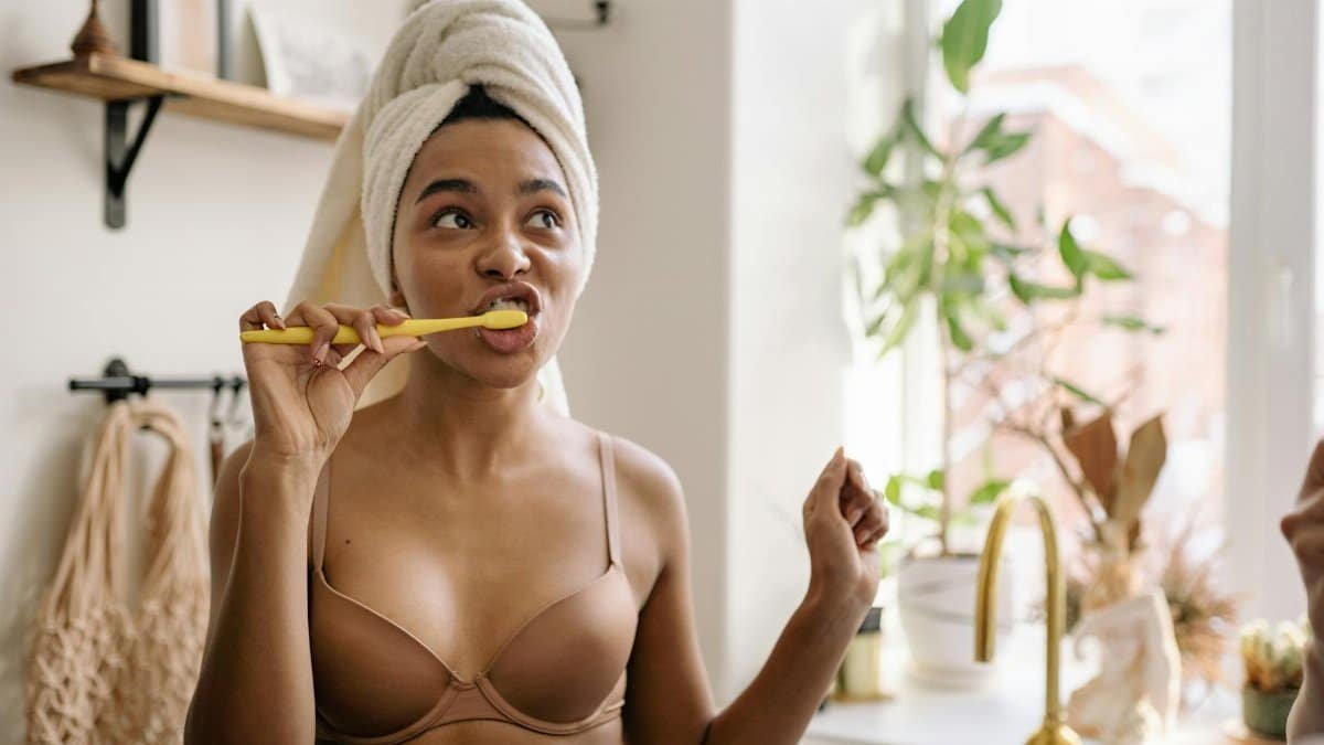 A young woman brushes her teeth, wrapped in a towel, enjoying morning self-care routine.