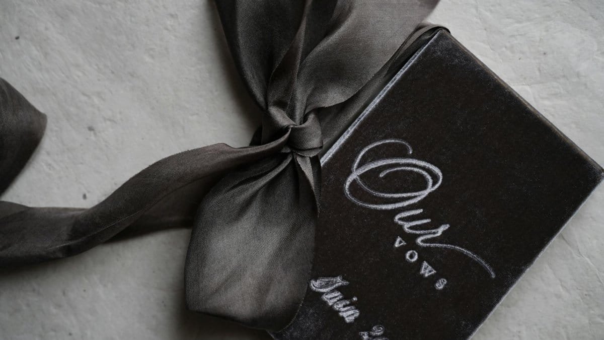 A vintage-style wedding vow booklet with elegant satin ribbon on textured surface.