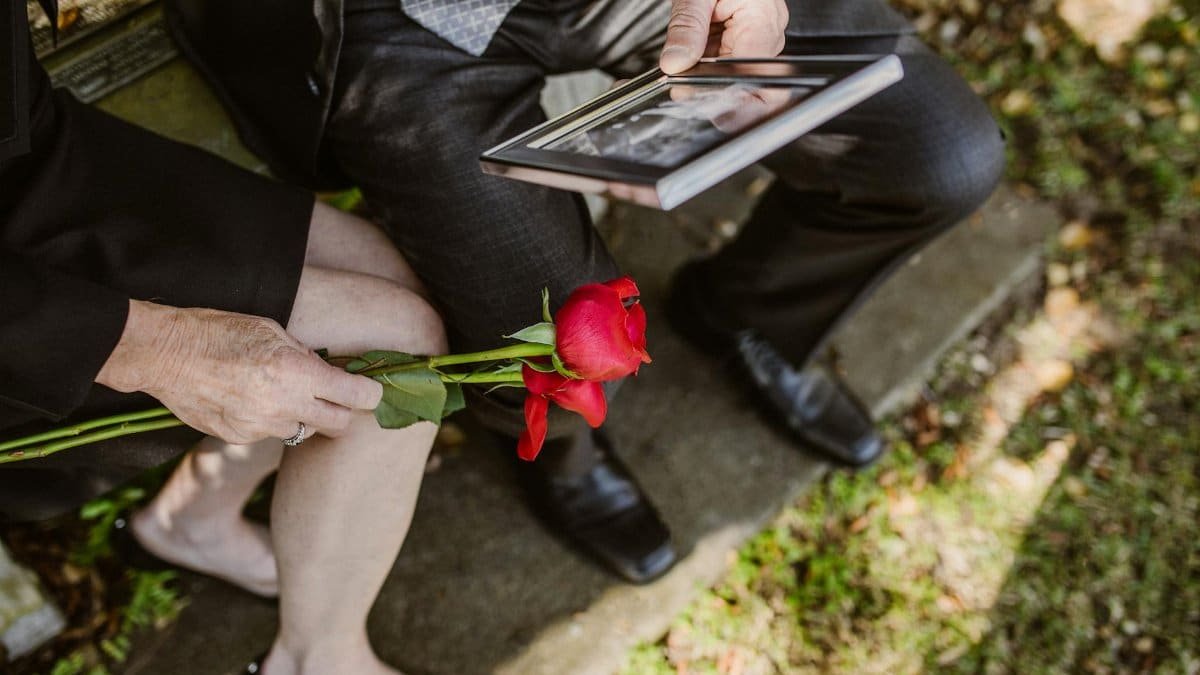 A grieving couple sitting with a red rose and a picture frame in their hands.