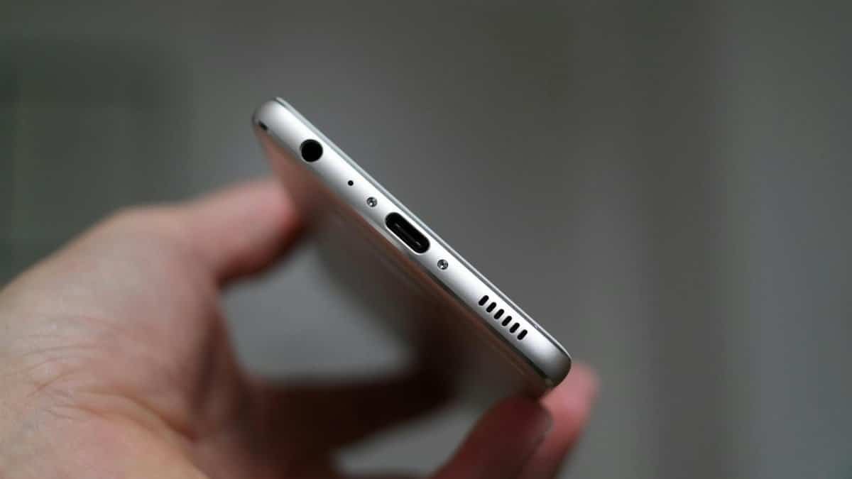 A close-up view of a person holding a smartphone, focusing on the charging port and headphone jack.