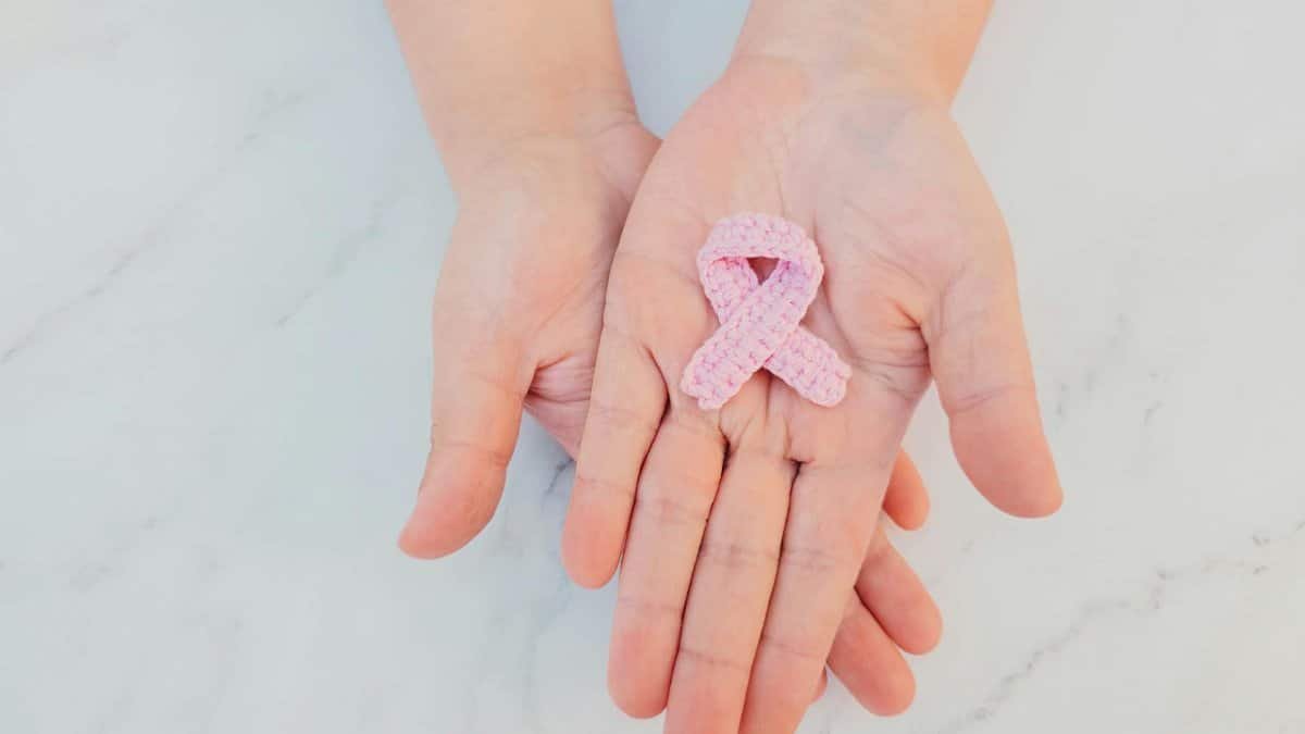Pink ribbon in hands symbolizing breast cancer awareness on marble background.