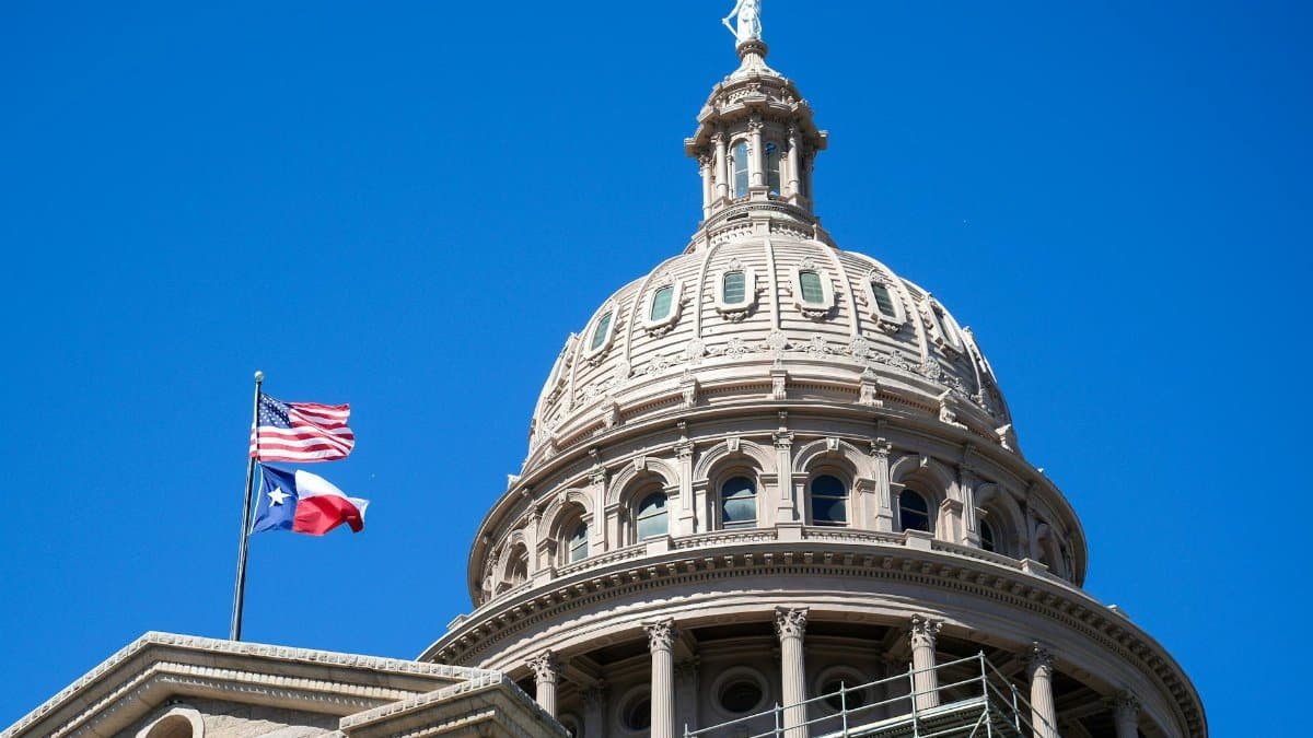 Close-up view of the Texas State Capitol dome in Austin with flags against a clear blue sky.