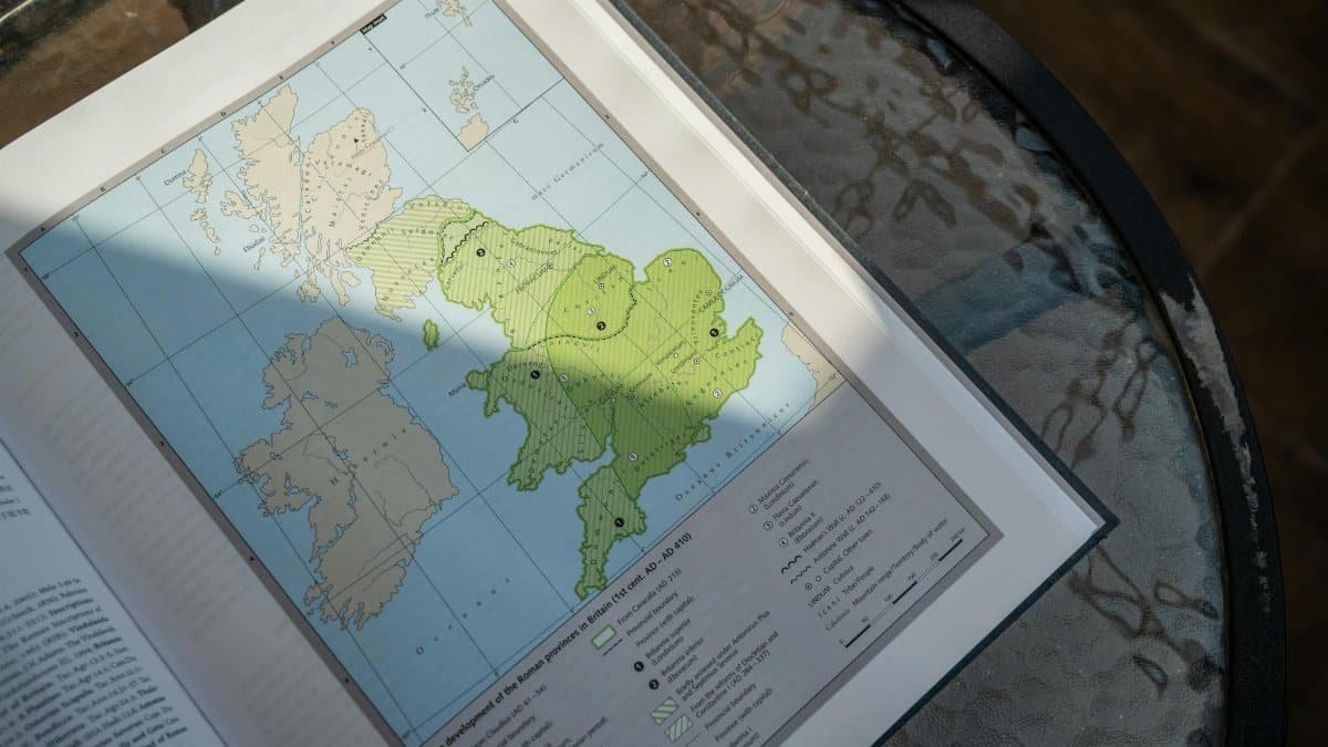 A detailed map of Roman Britain in an open book on a glass table.