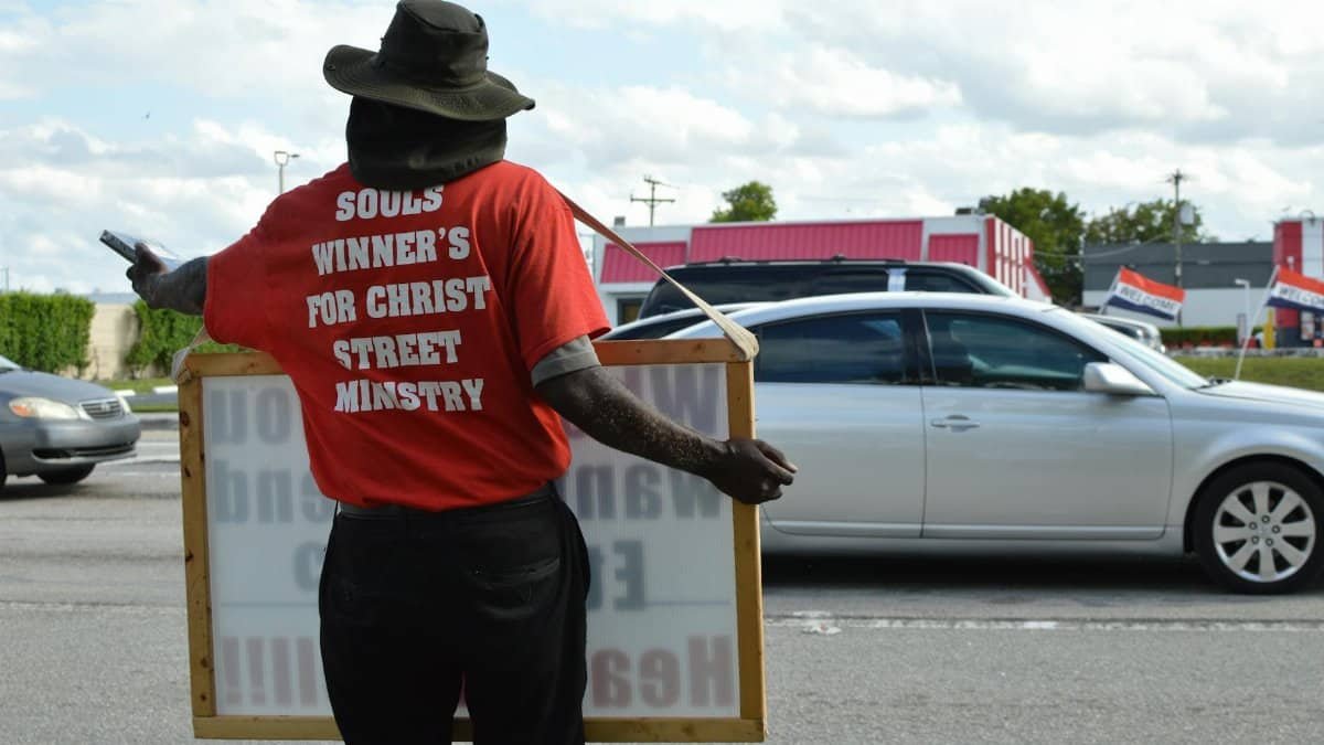 Individual holding ministry sign on busy street showcasing religious message