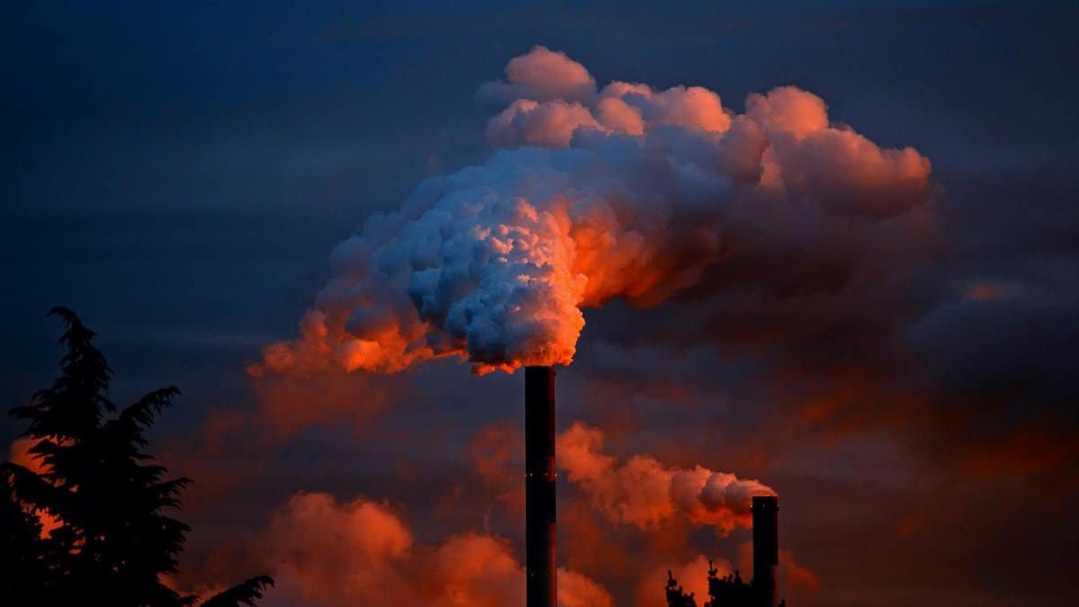 Smoke billows from industrial chimneys at sunset, highlighting pollution against a vibrant sky.