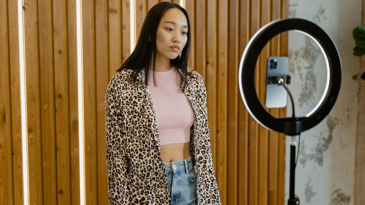 Asian female influencer recording content with ring light and smartphone indoors.